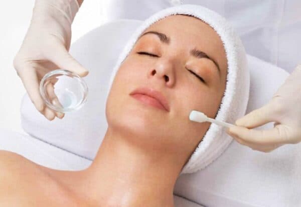 Gloved hands applying a skincare solution to a client's face with an applicator