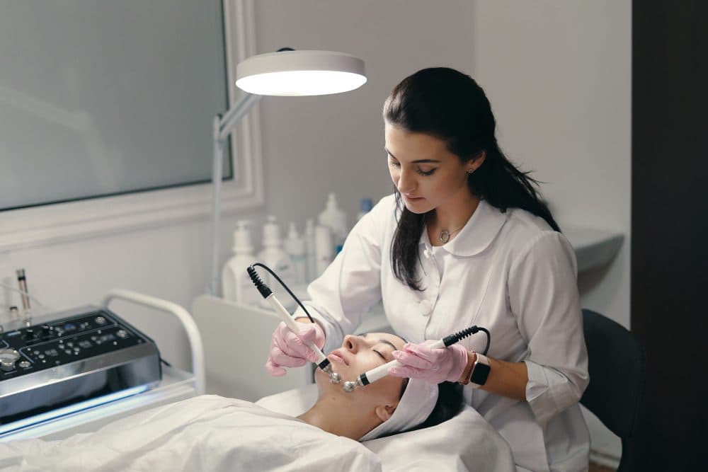 A practitioner delivering a radio frequency facial treatment with a handpiece under a clinic lamp